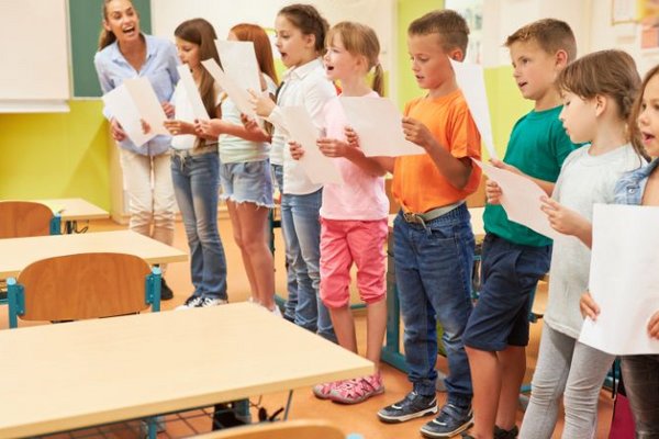 Eine Gruppe Grundschulkinder übt im Klassenzimmer mit einer Musikpädagogin singen