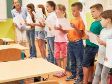 Eine Gruppe Grundschulkinder übt im Klassenzimmer mit einer Musikpädagogin singen