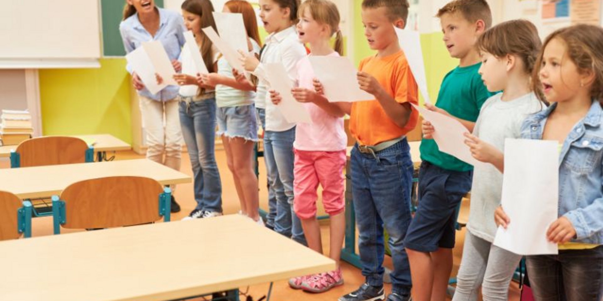 Eine Gruppe Grundschulkinder übt im Klassenzimmer mit einer Musikpädagogin singen