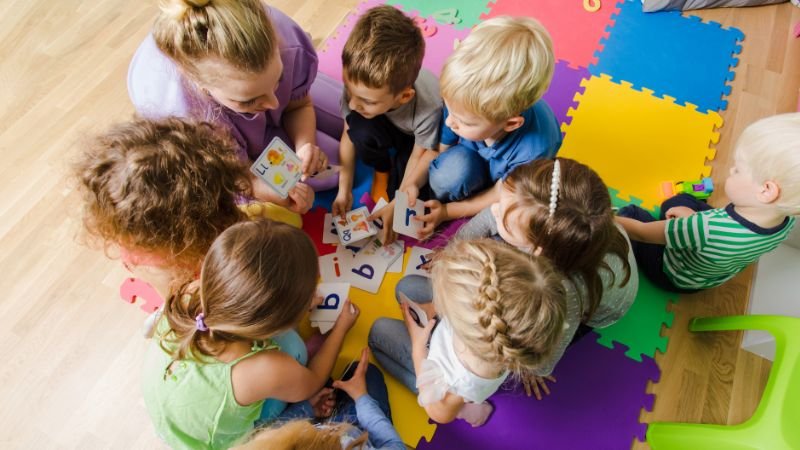 Erzieherin bespricht mit Kindergartenkindern Zahlenkärtchen im Sitzkreis